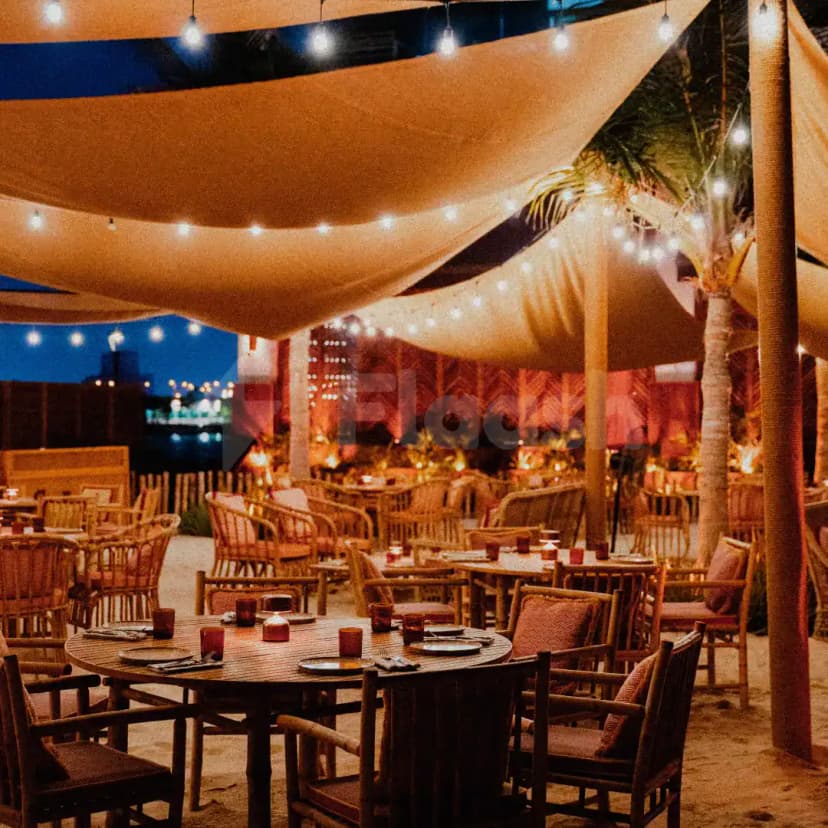 Rooftop terrace at Tagomago Dubai featuring a fabric canopy with string lights and palm trees over sand flooring