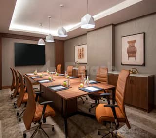 Boardroom at Swissotel Living Jeddah featuring a long wooden table, orange leather chairs, and a wall-mounted screen