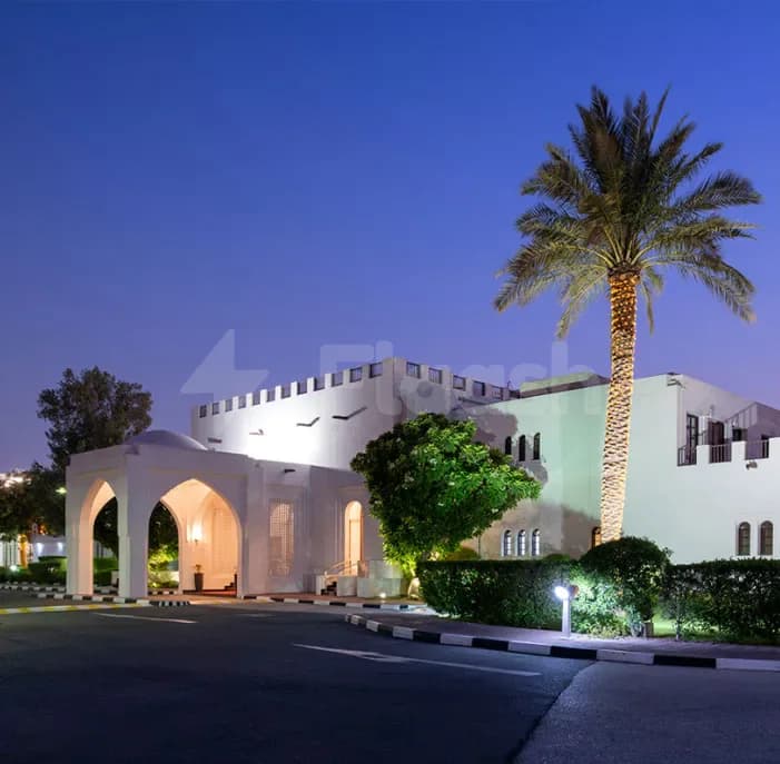 Hotel facade of Al Jewan Hall Doha featuring an arched entranceway and illuminated palm tree against a twilight