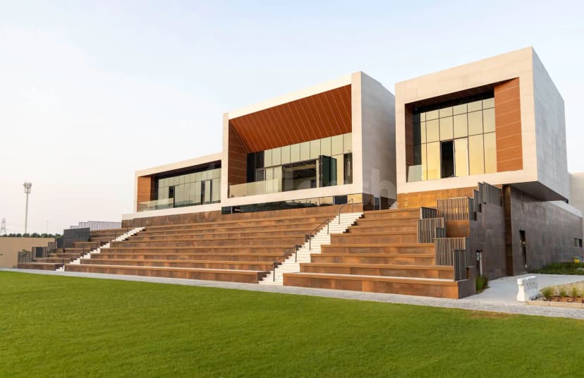 Tiered wooden steps lead up to the SEE Institute Dubai terrace, featuring a beige stone facade and rust-colored