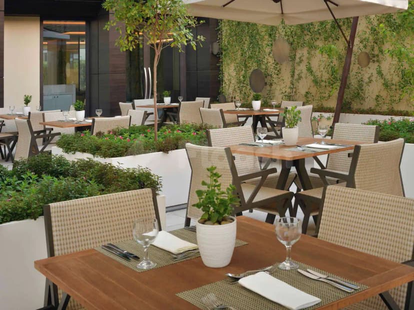Rooftop terrace at Rasoi By Vineet Jeddah featuring wooden tables with woven chairs, raised garden beds