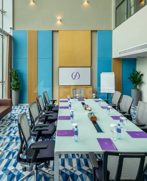 Boardroom at Flora Inn Hotel Dubai Airport featuring a long rectangular table with purple placemats and a yellow