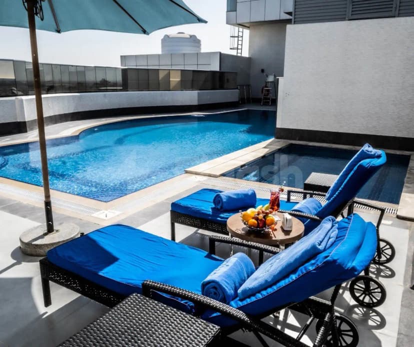 Rooftop pool at TIME Onyx Hotel Apartments Dubai featuring a curved blue pool, dark grey tiles, and lounge