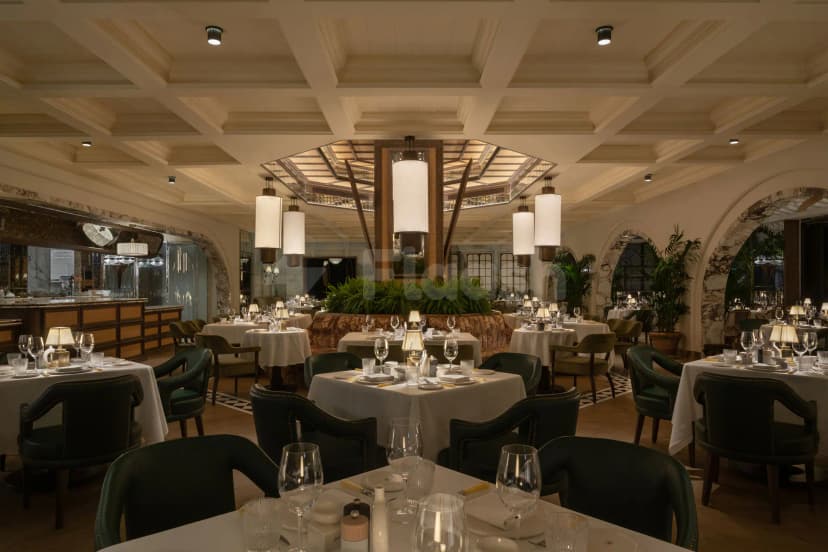 Restaurant interior at Ristorante Loren in Dubai featuring a coffered ceiling, central plant divider, and arched marble doorways
