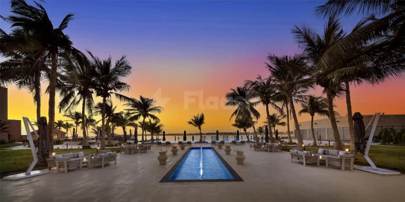 Terrace at Kempinski Sariya in Yanbu featuring a rectangular pool with fountain jet and palm trees at sunset