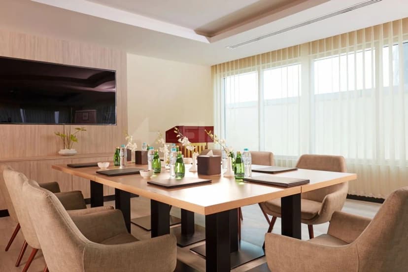 Boardroom at Treppan Hotel & Suites Dubai featuring a long wooden table, beige chairs, and a wall-mounted TV