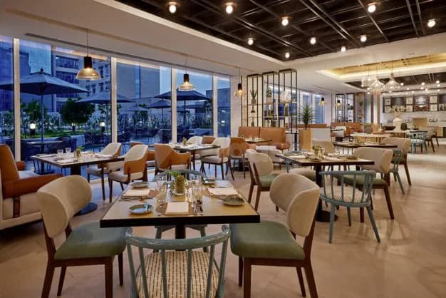 Restaurant at Courtyard Jubail in Al Jubail featuring modern dining tables, upholstered chairs, large windows overlooking an outdoor