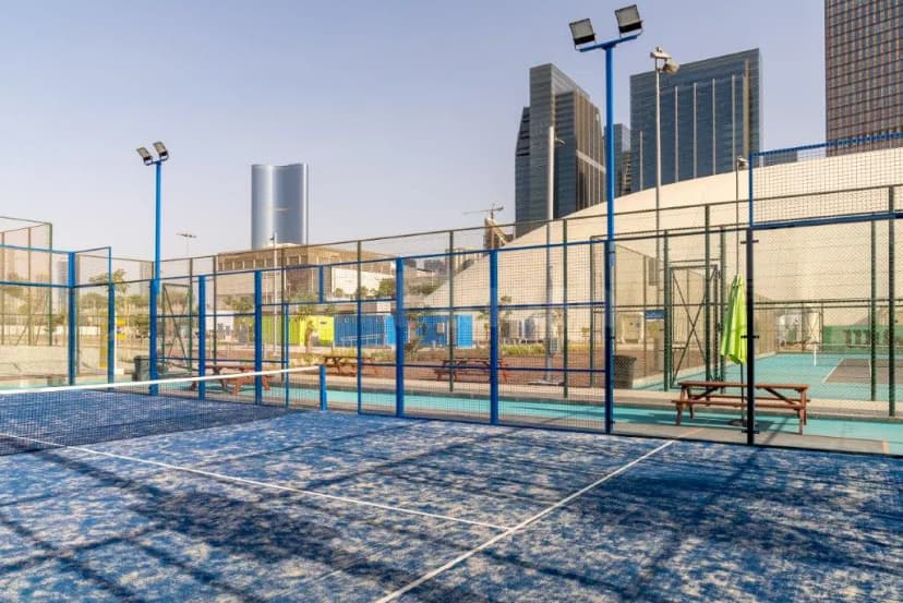 Blue tennis court at Active Al Maryah Island Sports & Recreation in Abu Dhabi with netted enclosure and floodlights