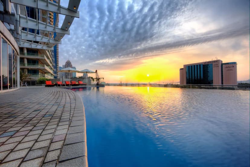 Rooftop terrace at Tamani Hotel Marina Dubai featuring an infinity pool and modern building facade under a sunset