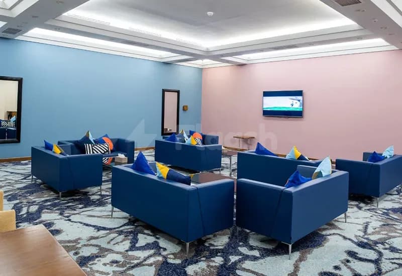 Meeting room at Al Jewan Hall Doha featuring blue leather sofas, a patterned carpet, and a mounted flat