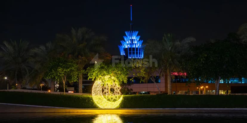 Illuminated crescent moon sculpture in landscaped garden at Dubai Silicon Oasis Authority, with palm trees and blue-lit building