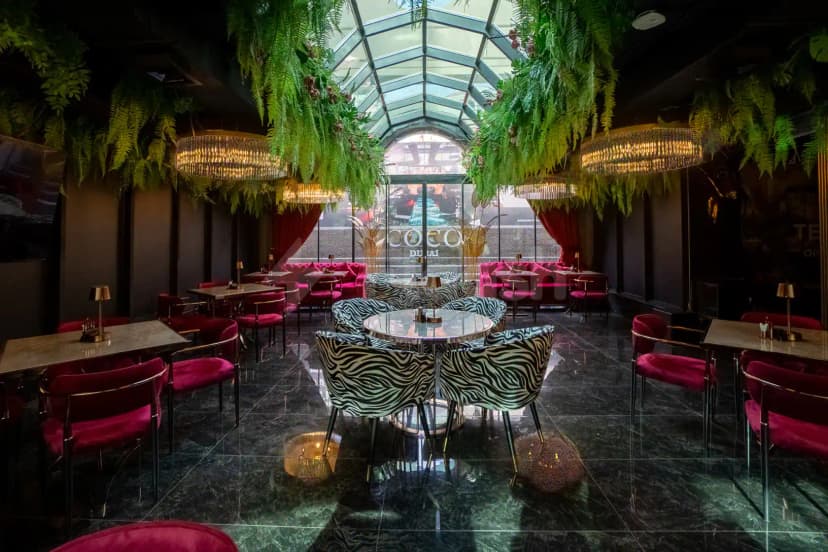 Indoor restaurant space at Coco Restaurant Al Murooj in Dubai featuring hanging green ferns and crystal chandeliers under