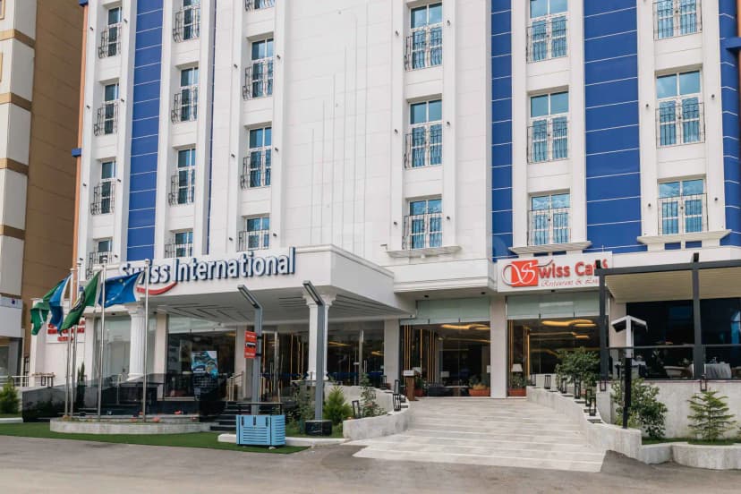 Hotel facade of Swiss International Taif featuring white columns, blue vertical panels, glass entrance, and flags on poles