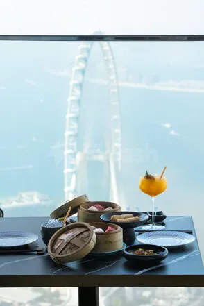 Rooftop terrace at Mott 32 Dubai with dim sum on a black marble table and a Ferris wheel