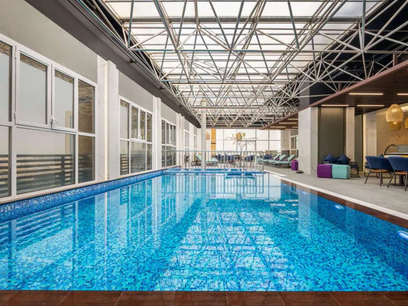 Indoor swimming pool at Mercure Riyadh Al Anoud featuring blue mosaic tiles and a glass roof with metal