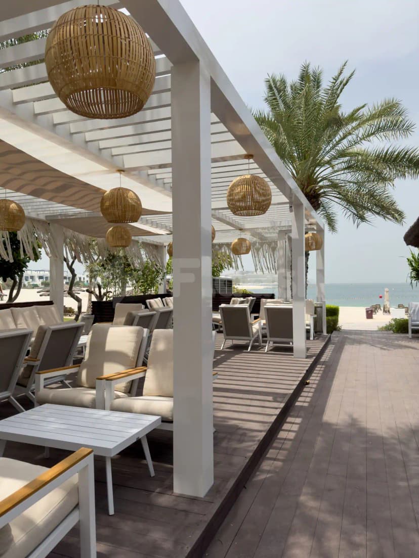 Terrace at Cabana On The Beach Palm Dubai featuring a white pergola, woven rattan pendant lights, and ocean