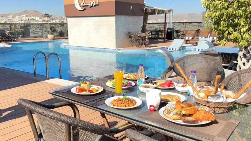 Rooftop terrace at Le Reve Hotel Taif featuring an outdoor breakfast table beside a swimming pool with mountain