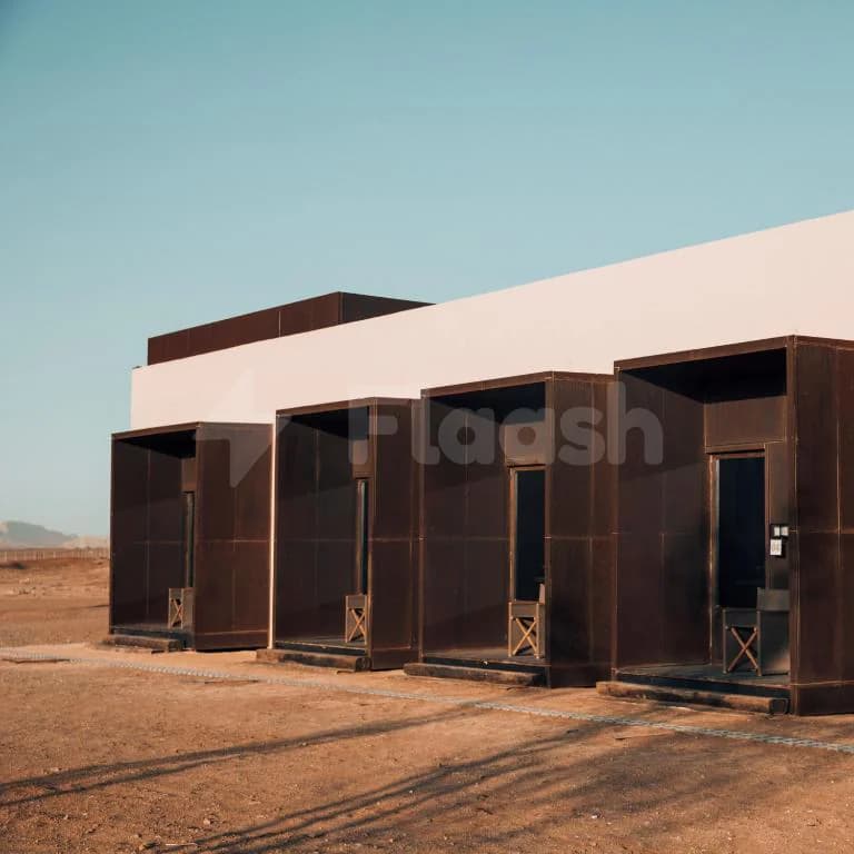 Al Faya Retreat facade in Sharjah features a white wall with rusted metal rectangular openings and wooden chairs