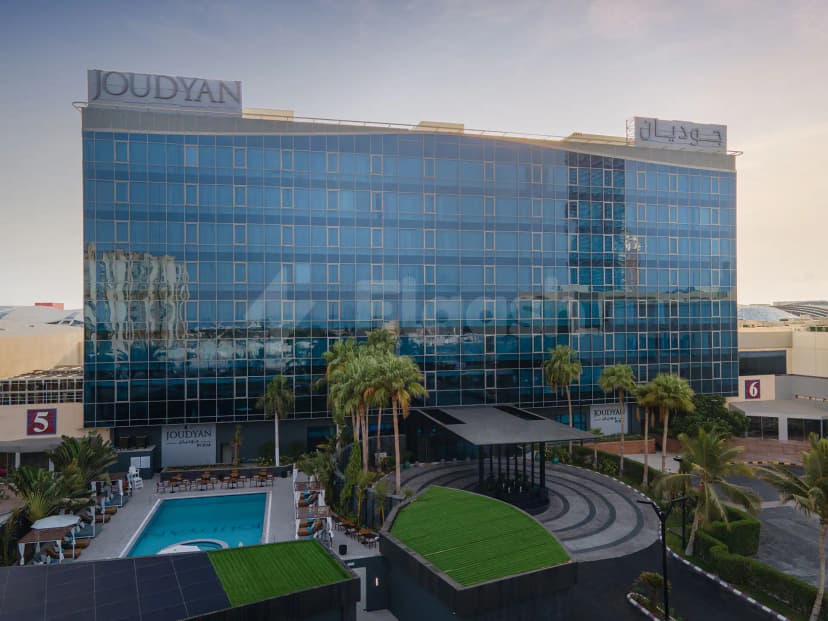 Hotel facade of Joudyan King Road Jeddah by Elaf featuring blue-tinted glass windows and palm trees