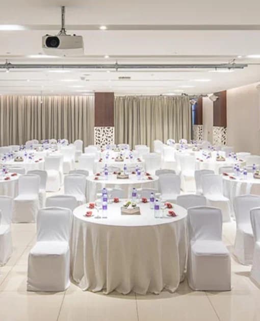 Ballroom at Flora Inn Hotel Dubai Airport set with round tables, white linens, chair covers, and a ceiling-mounted