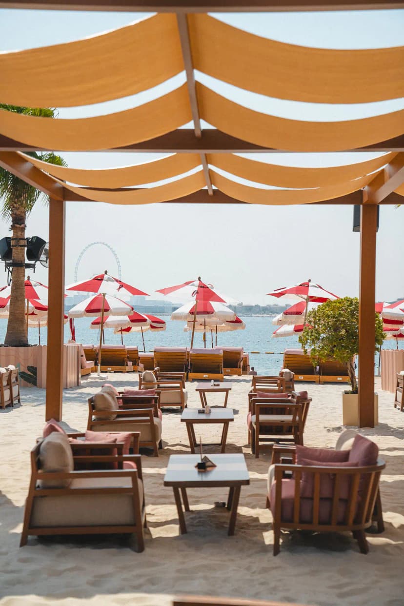 Terrace at February 30 in Dubai featuring a wooden pergola with beige fabric canopy and red-and-white umbrellas