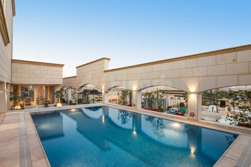 Rectangular swimming pool at Intercity Hotel Riyadh with beige stone surround and arched colonnade overlooking the city skyline