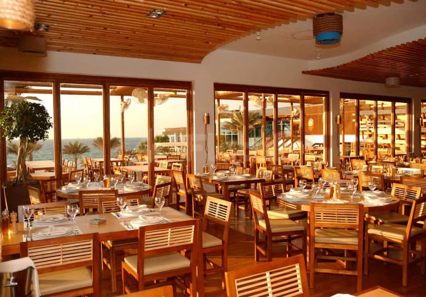 Flooka Restaurant Dubai dining area with wooden ceiling and large windows overlooking the ocean and palm trees