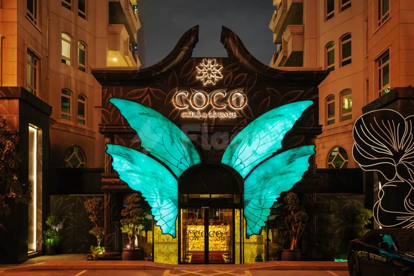 Illuminated butterfly wings flank the black ornate facade of Coco Restaurant Al Murooj in Dubai, featuring gold lettering