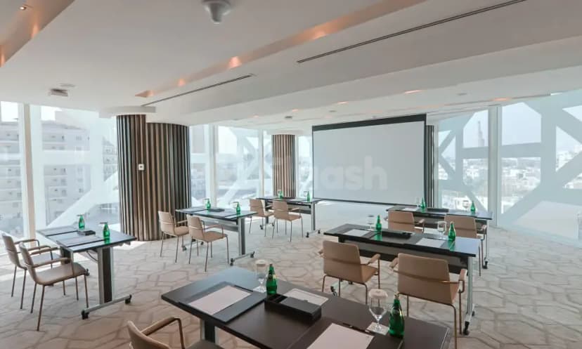 Meeting room at Shaza Doha with floor-to-ceiling windows offering city views and a large projection screen