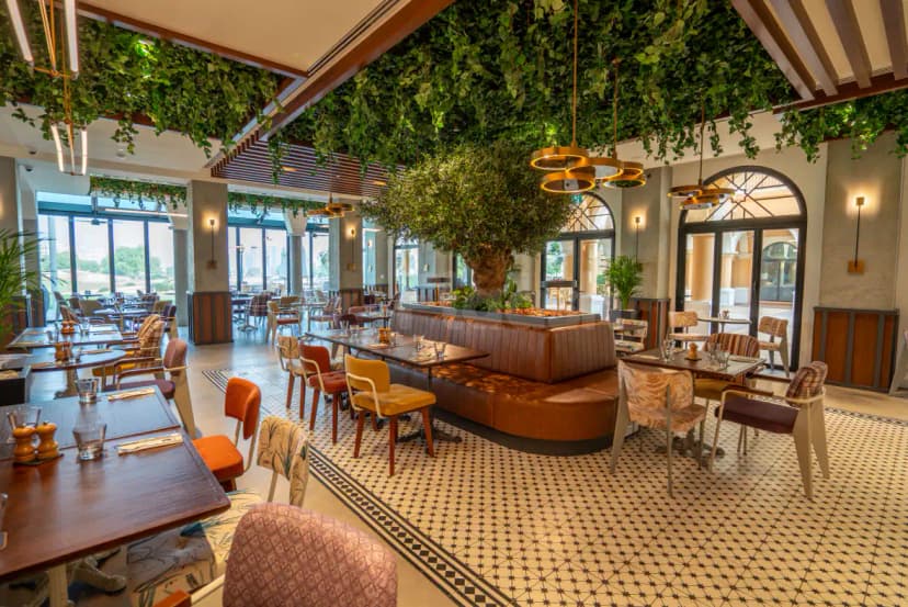 Indoor dining space at The Els Club Dubai Sports City featuring a large olive tree centerpiece and hanging