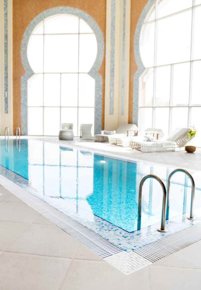 Indoor swimming pool at Shaza Riyadh featuring blue mosaic tiles, a metal ladder, and large arched windows
