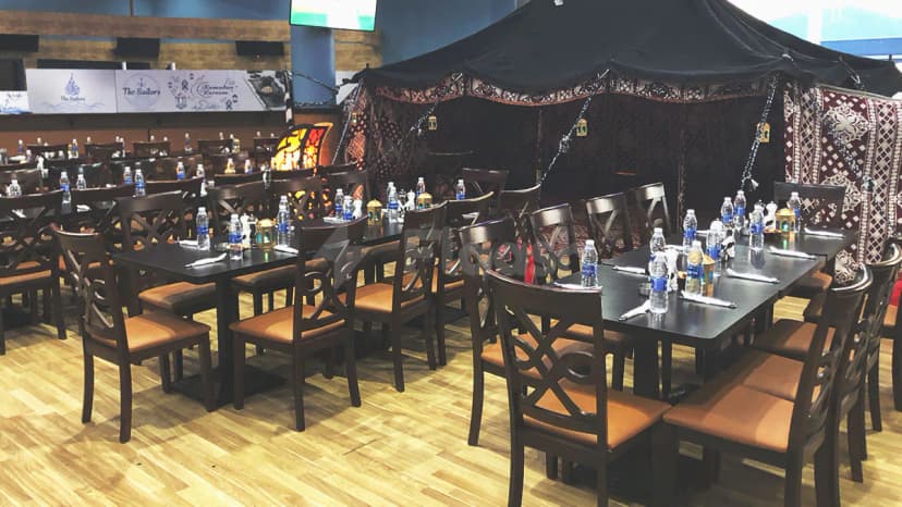 Restaurant interior at The Sailors Fujairah featuring dark wooden tables, brown chairs with orange cushions, and a black