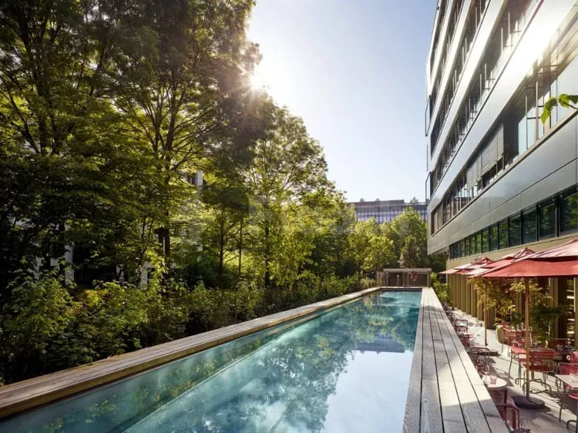 Rectangular swimming pool at Ernst Biergarten Restaurant Dubai, flanked by a wooden deck and a glass-walled building