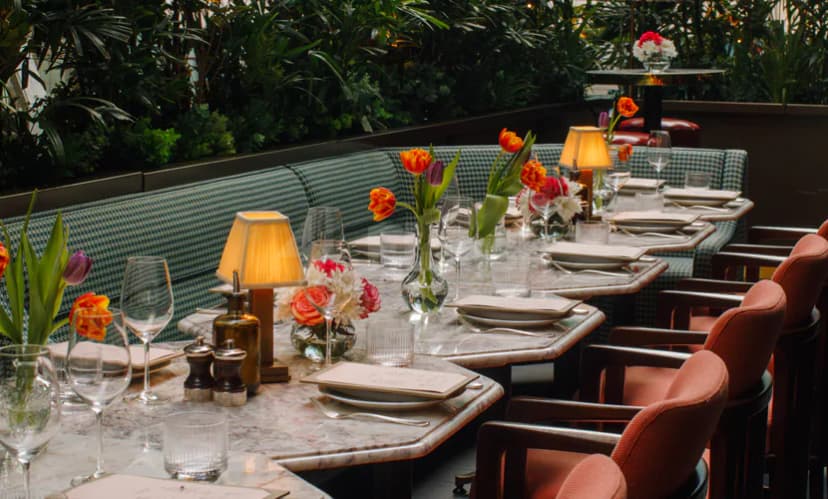 Restaurant at Alaya Dubai featuring marble tables, green checkered booths, and orange tulip centerpieces under warm ambient lighting