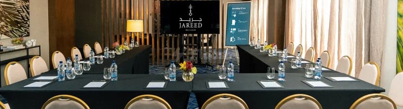 Boardroom at Jareed Hotel Riyadh set in U-shape with black tablecloth, beige chairs with gold frames, and floral