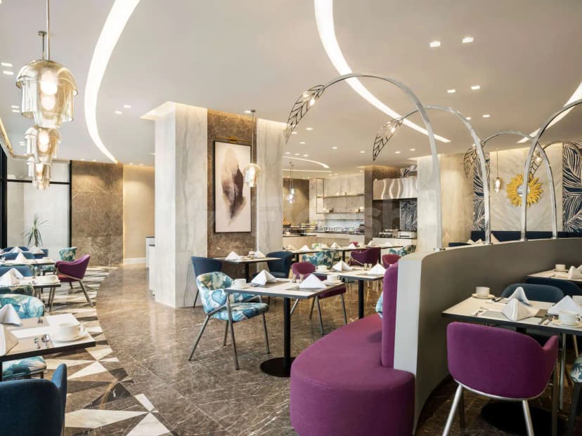 Restaurant at Mercure Riyadh Al Anoud featuring curved purple banquettes, marble flooring with geometric patterns, and arched metal