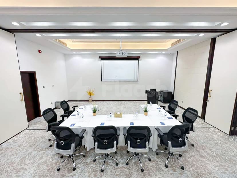 Boardroom at Al Ain Palace Hotel in Abu Dhabi featuring a rectangular table with chairs, projector, and screen