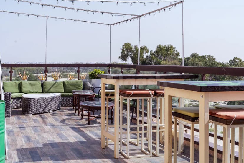 Rooftop terrace at Al Ghazal Golf Club in Abu Dhabi featuring wooden flooring, wicker seating with green cushions