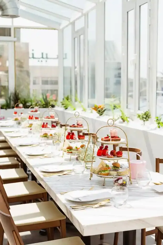 Long white marble dining table at Society Restaurant Abu Dhabi with gold three-tier serving stands and potted green