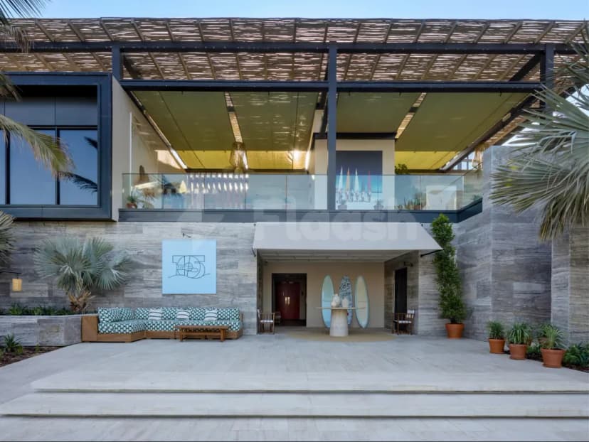 Entrance hall of La Cantine Beach in Dubai featuring a stone wall, wooden pergola overhead, and surfboards displayed