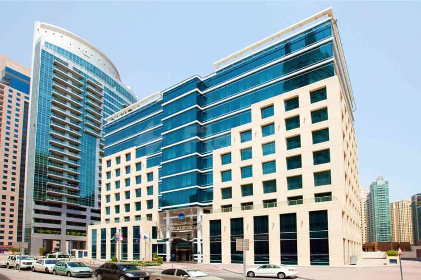 Hotel facade of Marina Byblos Hotel in Dubai featuring blue glass panels and beige stone cladding