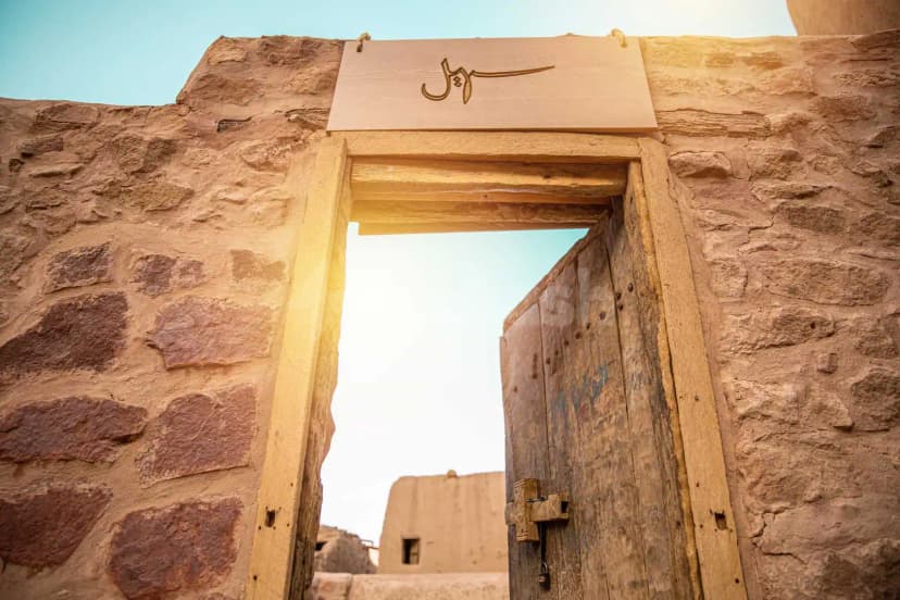 Stone wall facade of Suhail Arabic Restaurant in Riyadh featuring a weathered wooden door and Arabic calligraphy signboard