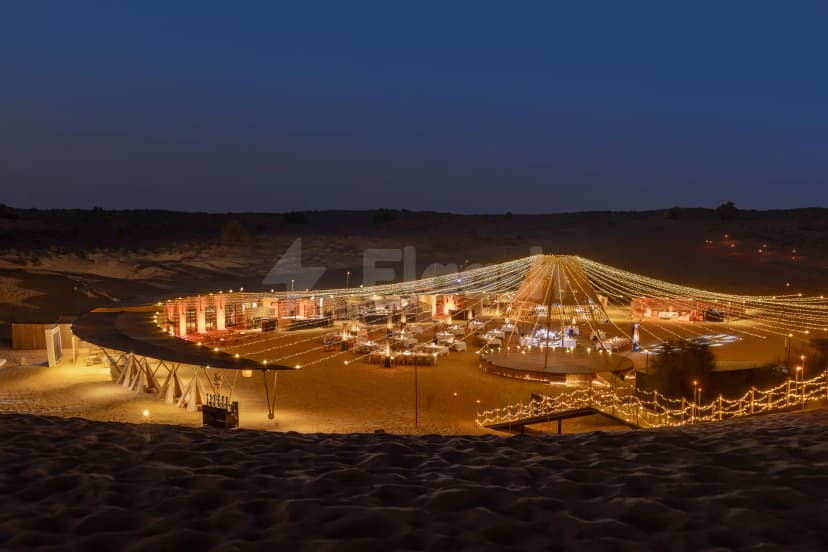Circular stage with wooden canopy and string lights at Nara Desert Escape in Dubai, set on sand under
