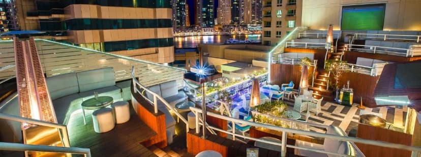 Rooftop terrace at Marina Byblos Hotel Dubai featuring modern lounge seating, wooden decking, and a city skyline view