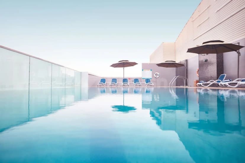 Rectangular swimming pool at Treppan Hotel & Suites Dubai with a glass safety barrier and black patio umbrellas