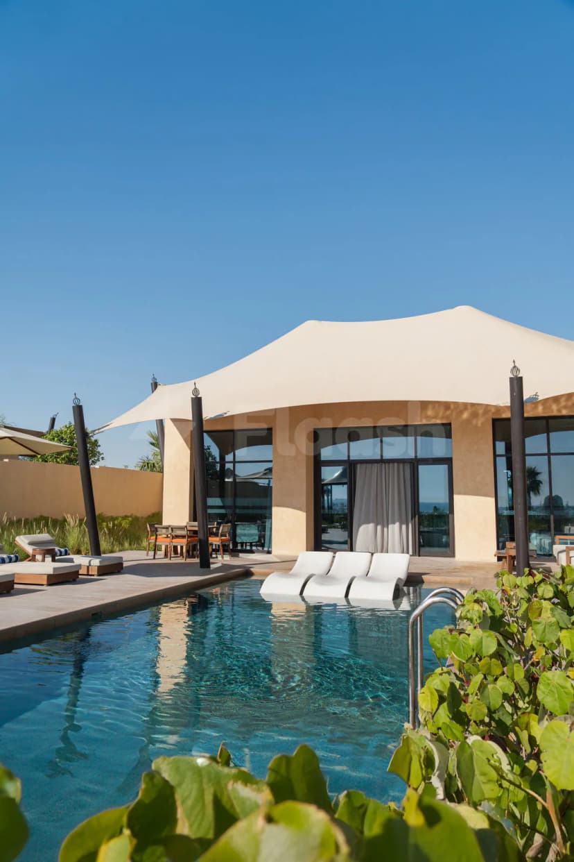 Rectangular swimming pool at Bab Al Nojoum Hudayriyat Camp in Abu Dhabi under a beige fabric canopy