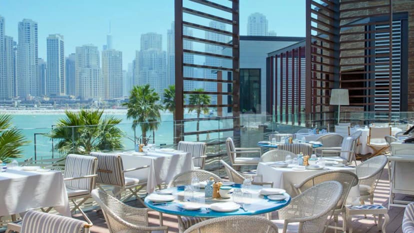 Rooftop terrace at Alici Restaurant Dubai featuring white tablecloths, wicker chairs, and a panoramic view of the Dubai