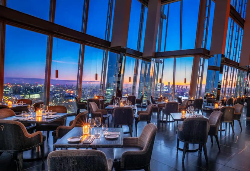 Restaurant interior at Hutong Dubai with floor-to-ceiling windows overlooking the city at twilight, set tables with candle