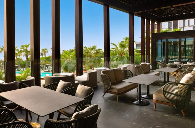 Rooftop terrace at TakaHisa Restaurant Dubai featuring modern lounge seating and large glass windows overlooking palm trees
