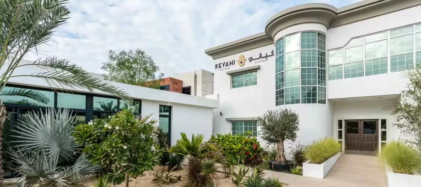 Hotel facade of Keyani Wellness in Dubai featuring a curved glass window and landscaped garden with palm trees